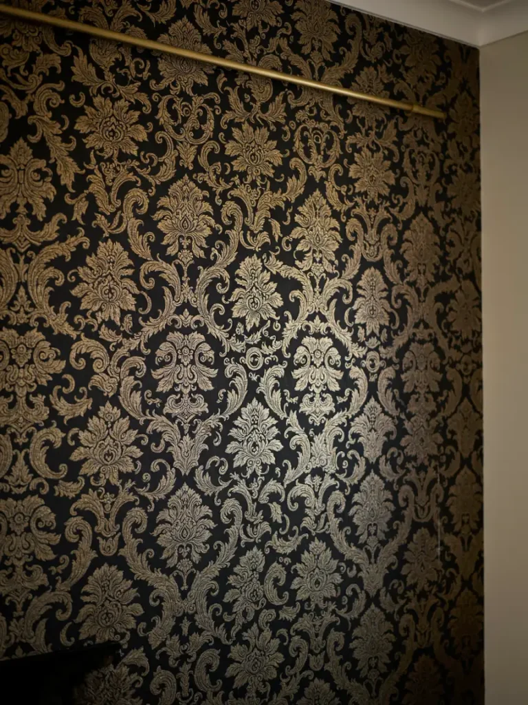 A close up of black and gold damask wallpaper texture, ideally applied to one accent wall.