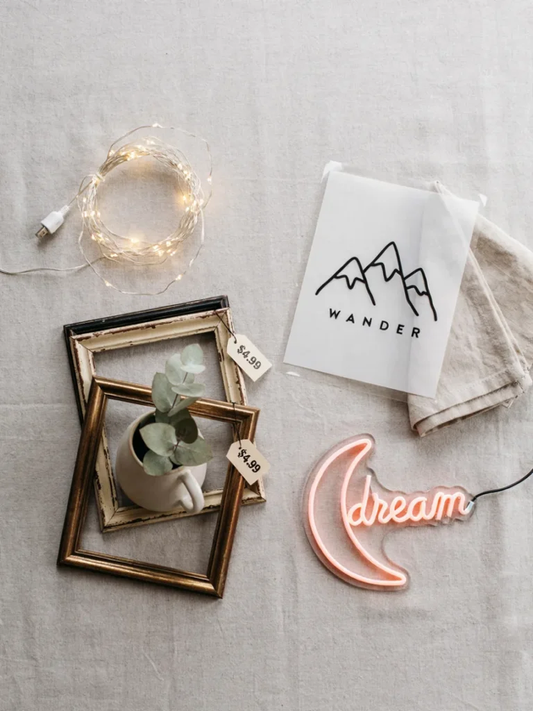 A flat lay of budget friendly decor items including string lights, a peel and stick decal, thrifted frames, and a small neon sign