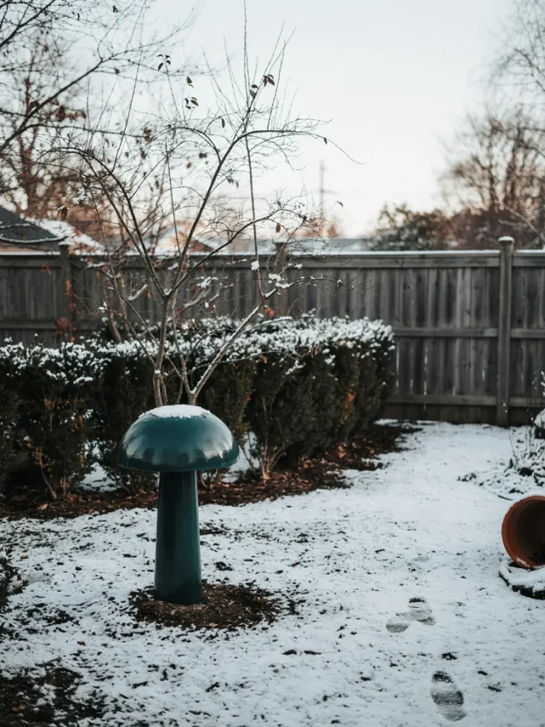 A powder coated metal mushroom statue standing in a garden dusted with light snow, showing cold weather durability