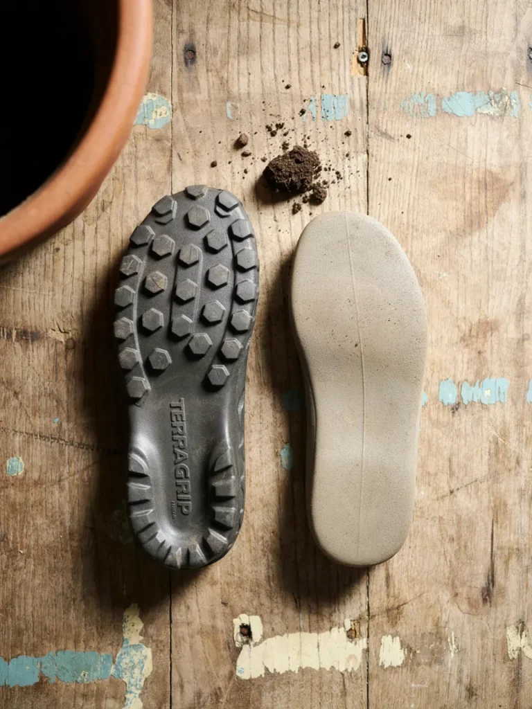 Close up underside shot of a gardening clog sole showing deep tread pattern, next to a smooth soled shoe for contrast, highlighting grip differences
