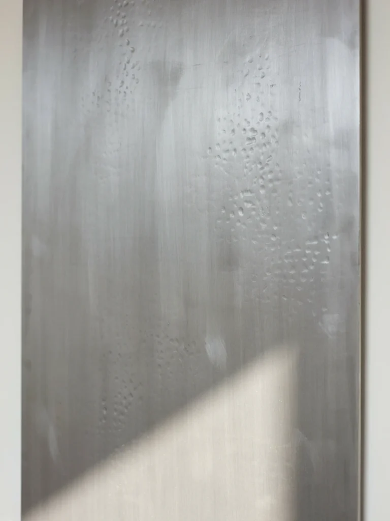 Close up detail shot of a textured metal wall art panel, showing how light catches the brushed or raw metal surface. Should highlight the material quality