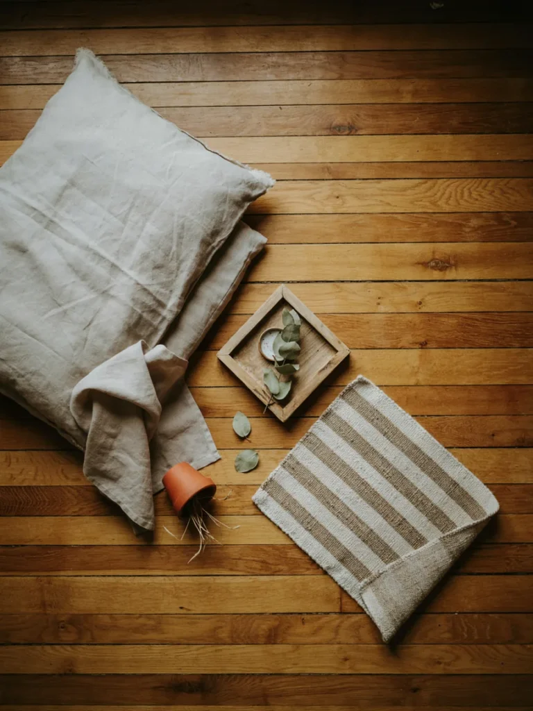 Flat lay of budget friendly styling pieces, a linen duvet cover, a small unfinished wood tray, and a woven rug swatch, soft neutral styling on a wooden surface