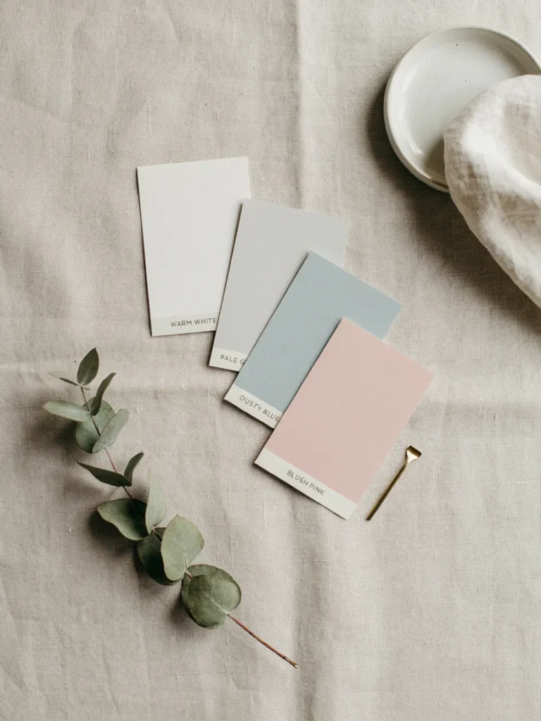 Flat lay of paint swatches in warm white, pale grey, dusty blue, and blush pink arranged on a neutral surface, soft elegant color palette comparison