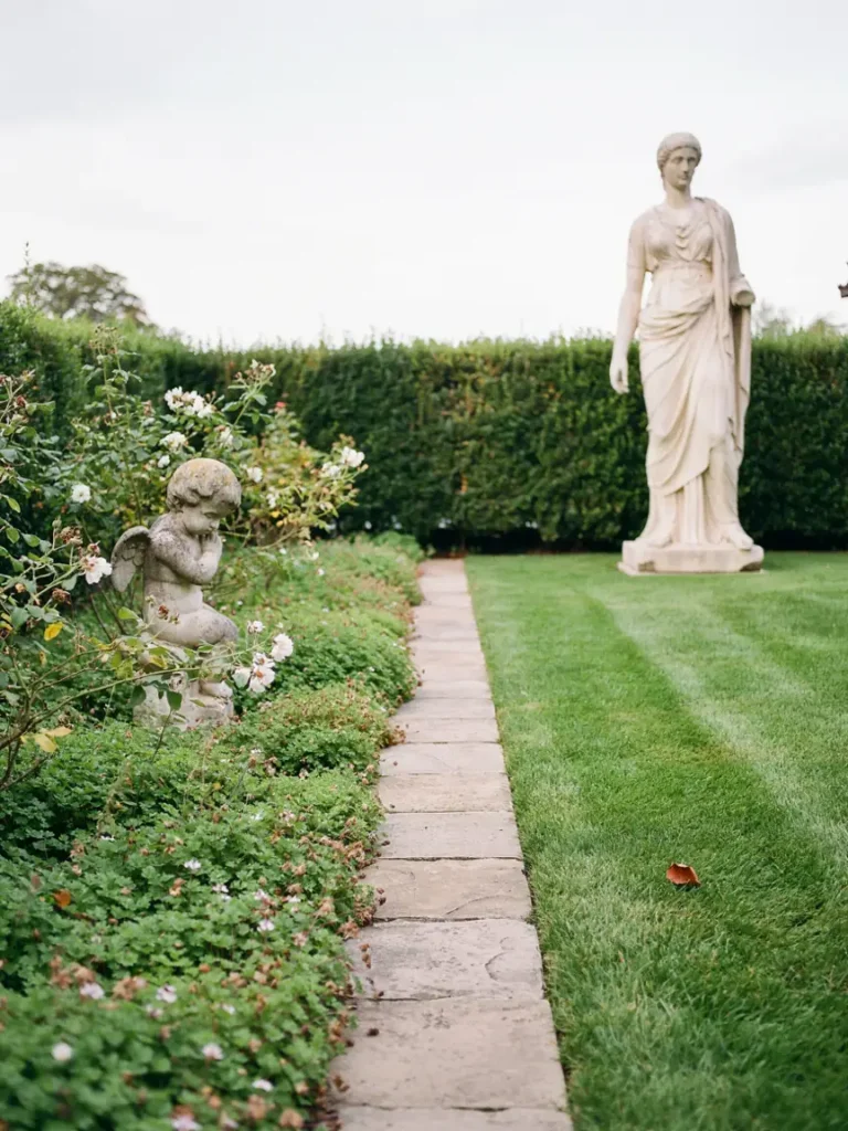 Side by side comparison of a small statue tucked among low ground cover and a larger statue standing alone in an open lawn corner, illustrating scale