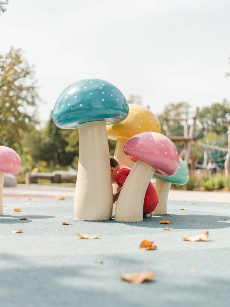 A cluster of bold turquoise, yellow, and hot pink mushroom statues in a children's outdoor play area.