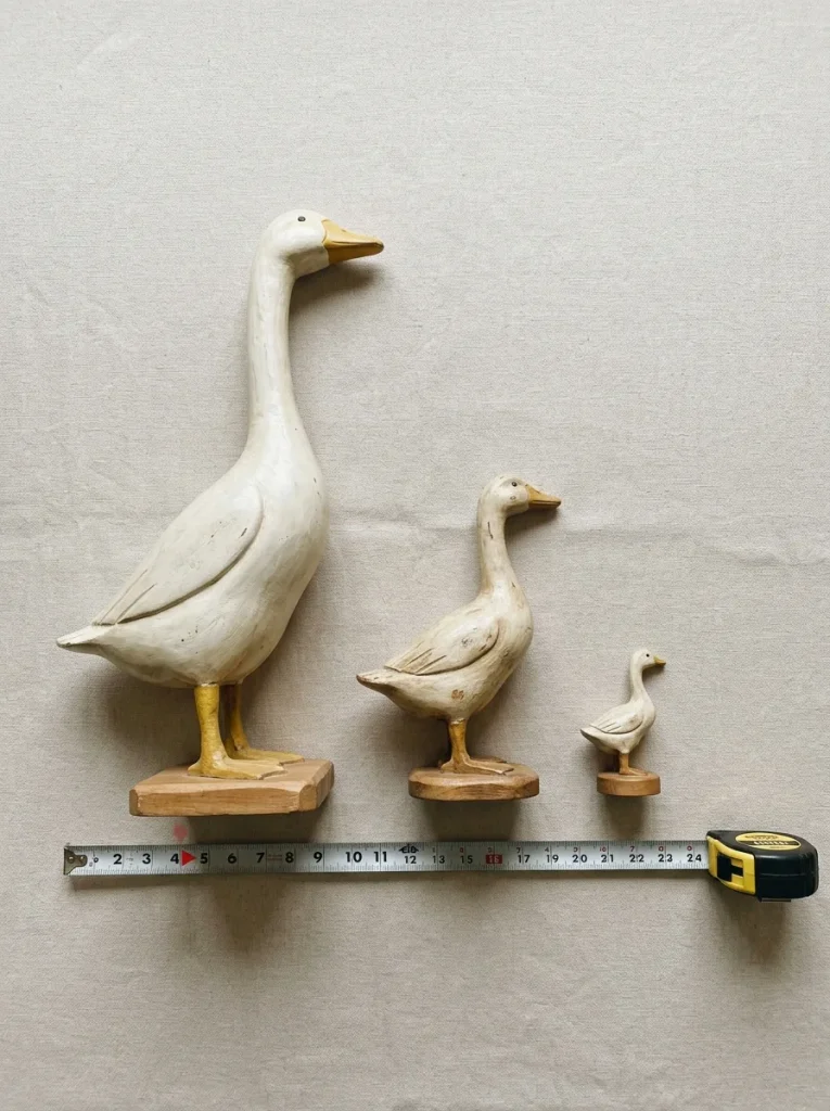 Three goose statues in different sizes with a tape measure for choosing a porch goose